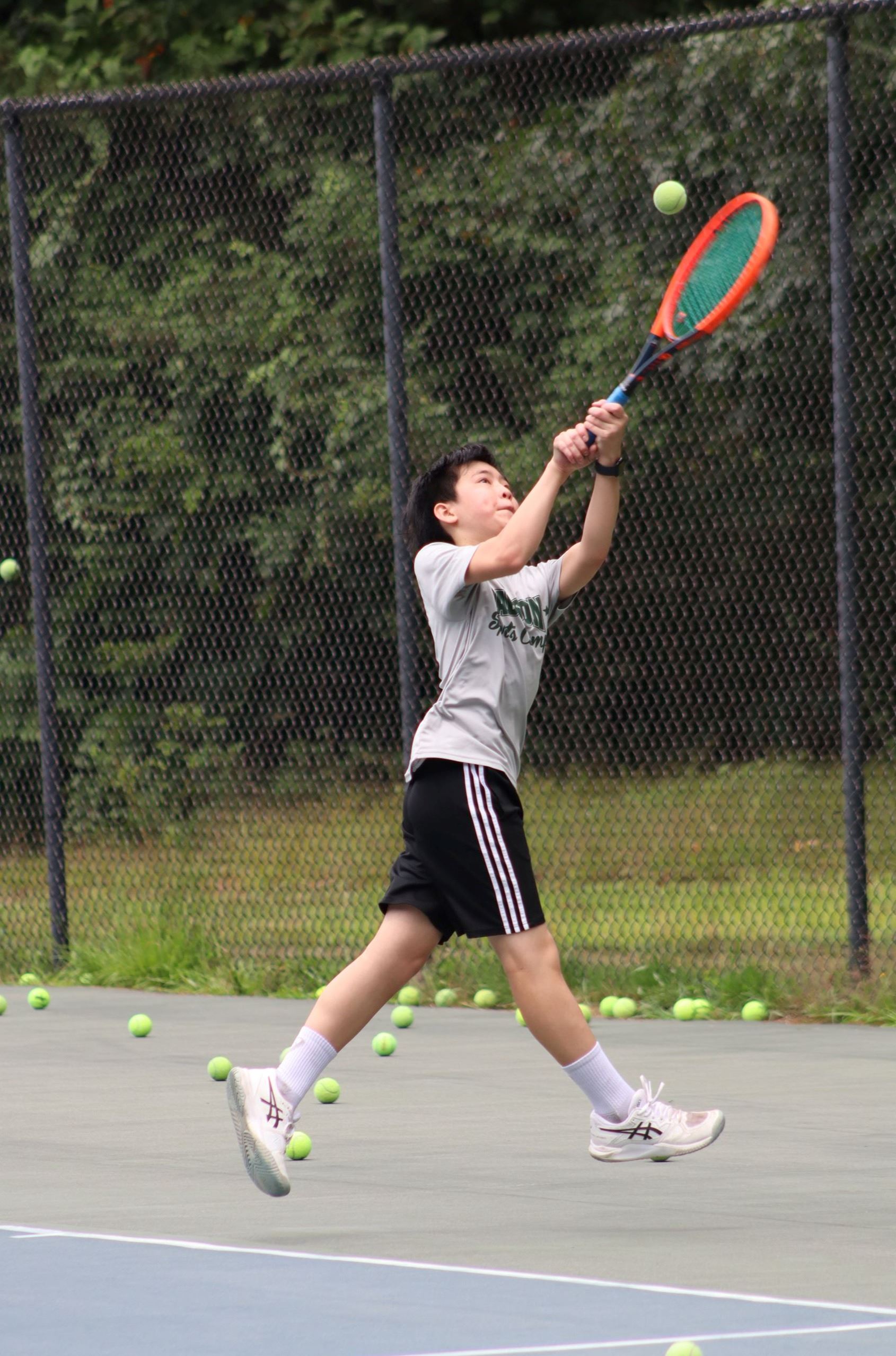 Photo of child reaching out to hit ball with tennis racket 